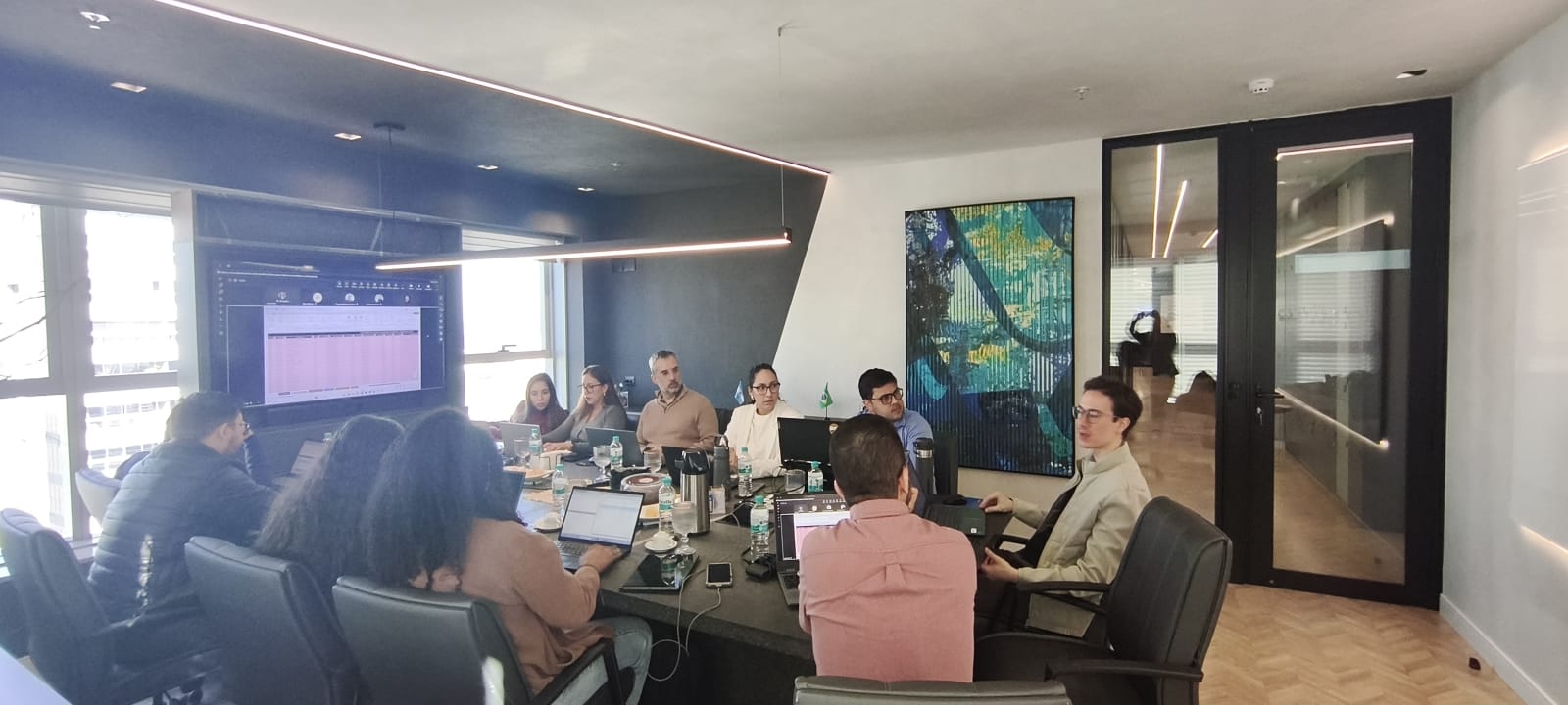 Sala de reunião de um cliente durante o treinamento in-company, com o time em volta da mesa e a planilha projetada na tela